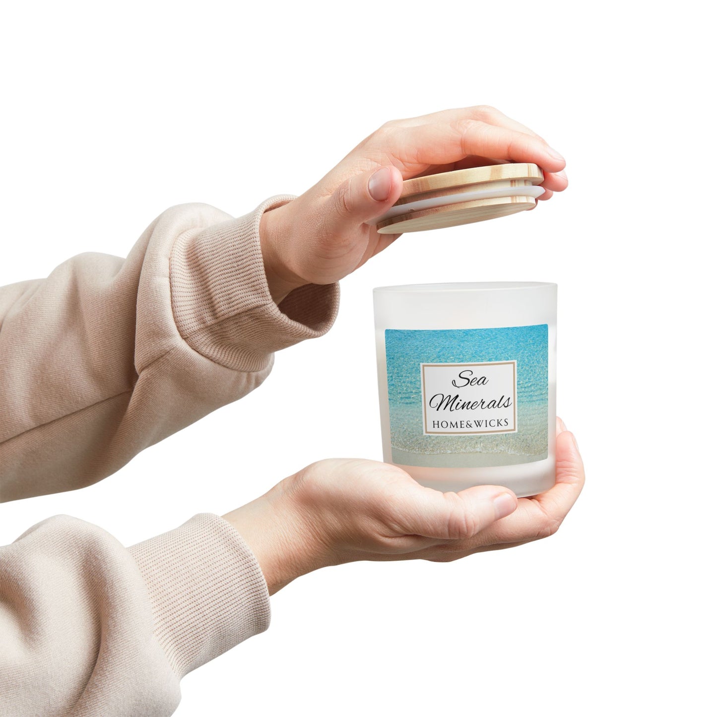 Person holding a candle labeled 'Sea Minerals' by Home & Wicks on a white background