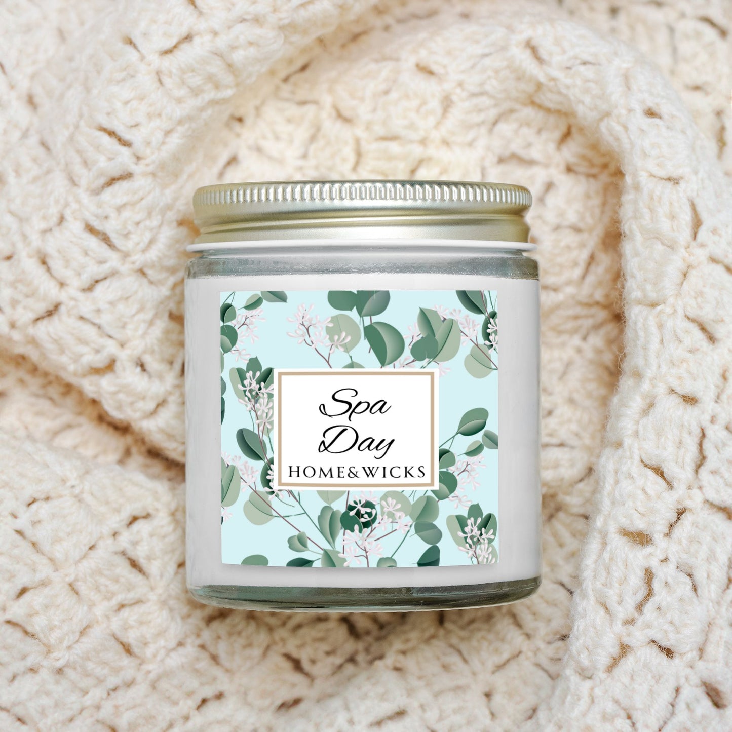 Spa Day candle by Homes & Wicks in a clear candle jar with gold lid with a eucalyptus floral label on a white background on a textured beige blanket background