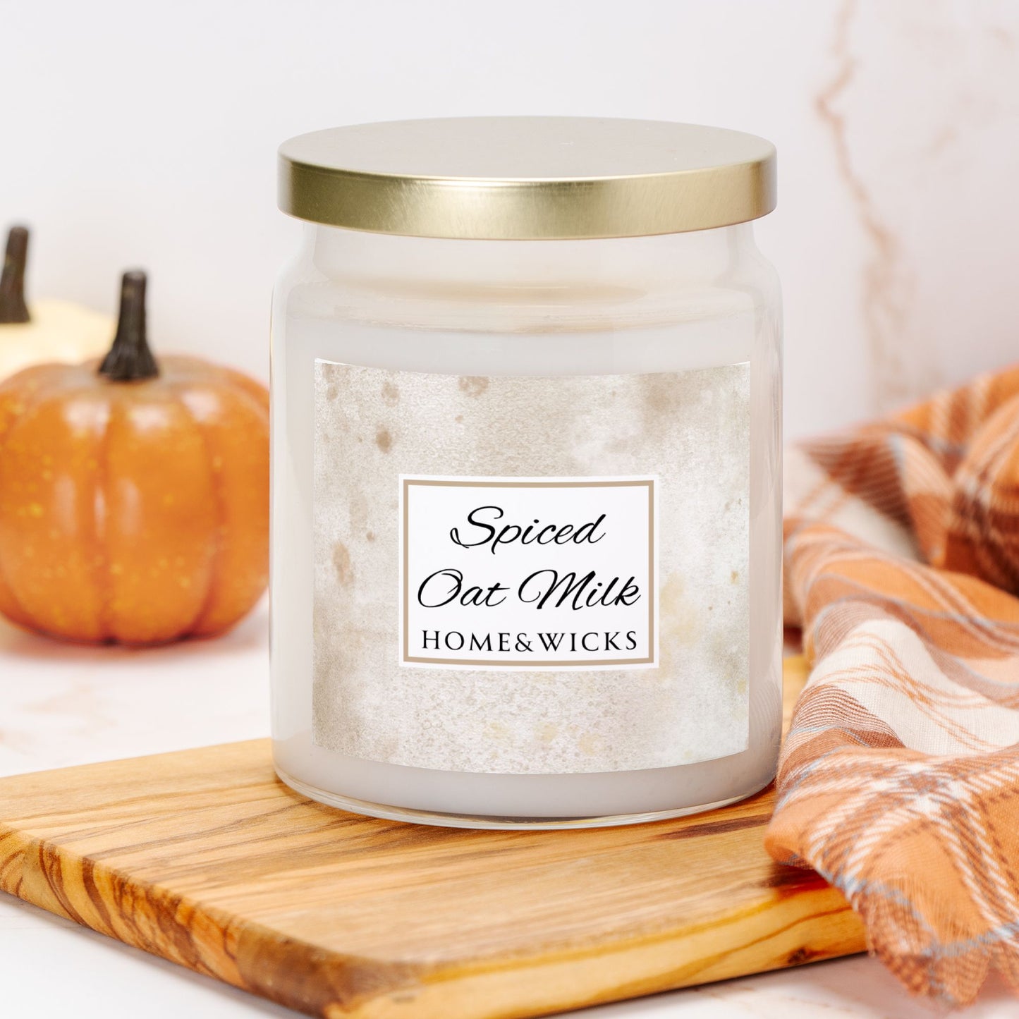 Candle jar labeled 'Spiced Oat Milk' by Home & Wicks on a wooden board with pumpkins and a plaid cloth in the background.