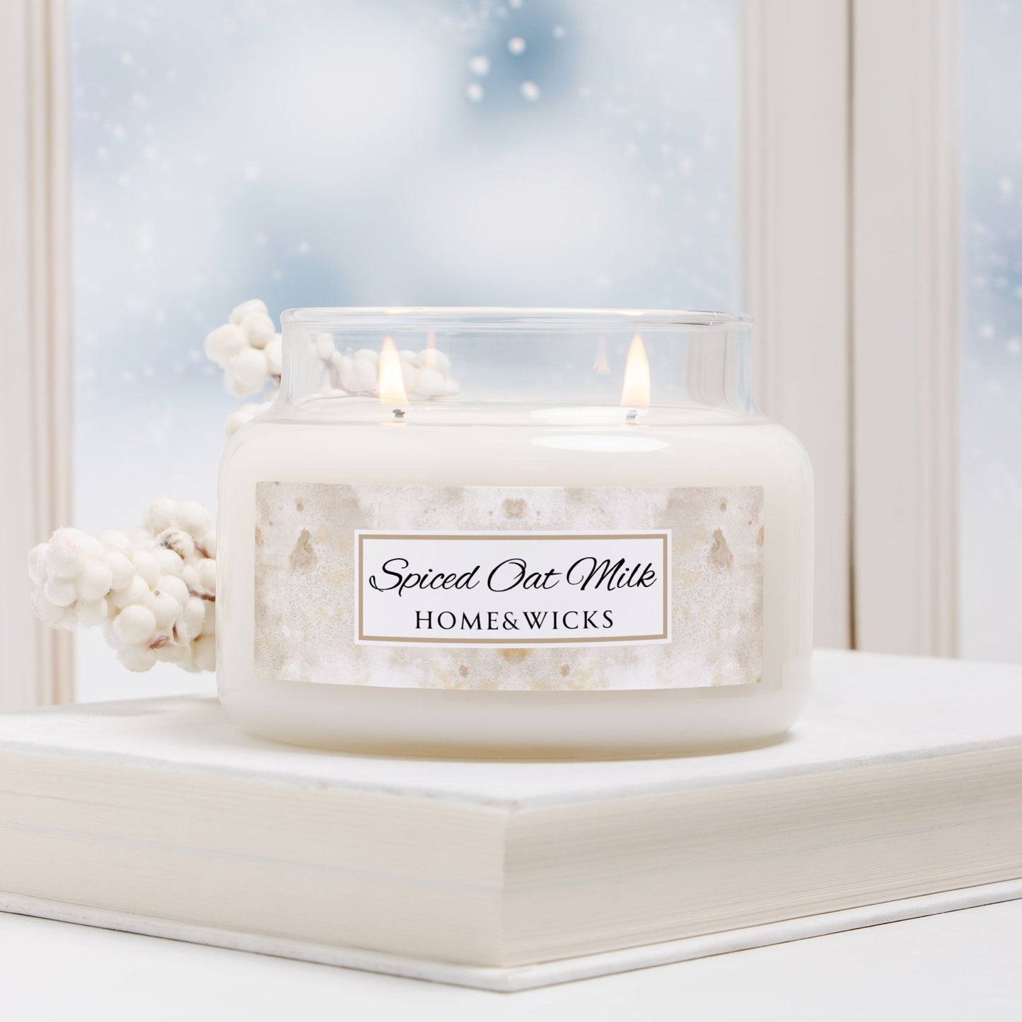 Candle labeled 'Spiced Oat Milk' by HOME&WICKS on a decorative stand with a snowy window background.