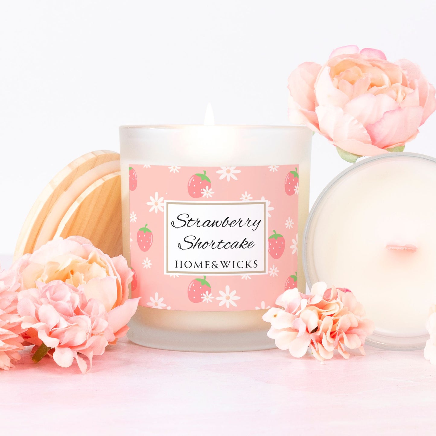 Candle with pink wood wick and labeled 'Strawberry Shortcake' by HOME&WICKS with floral decorations on a white background
