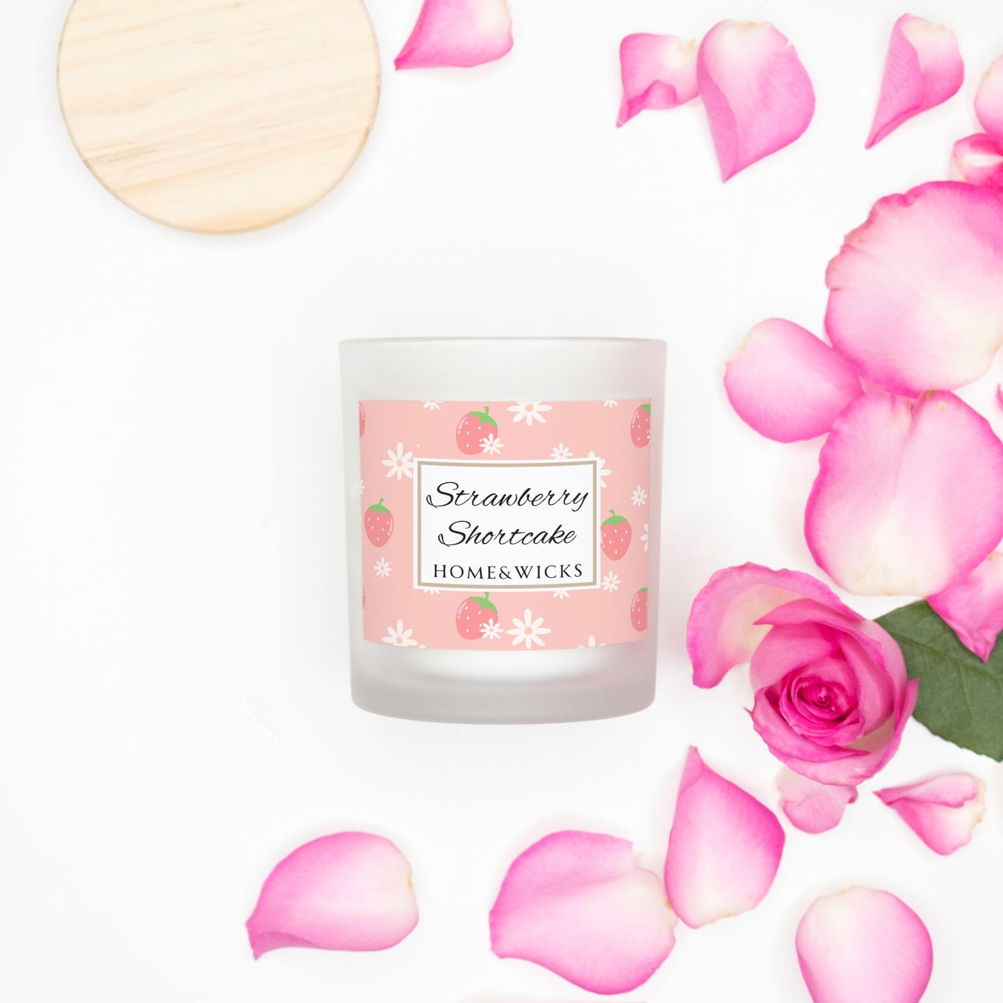 Home and wicks Strawberry Shortcake candle surrounded by pink roses and petals on a white background