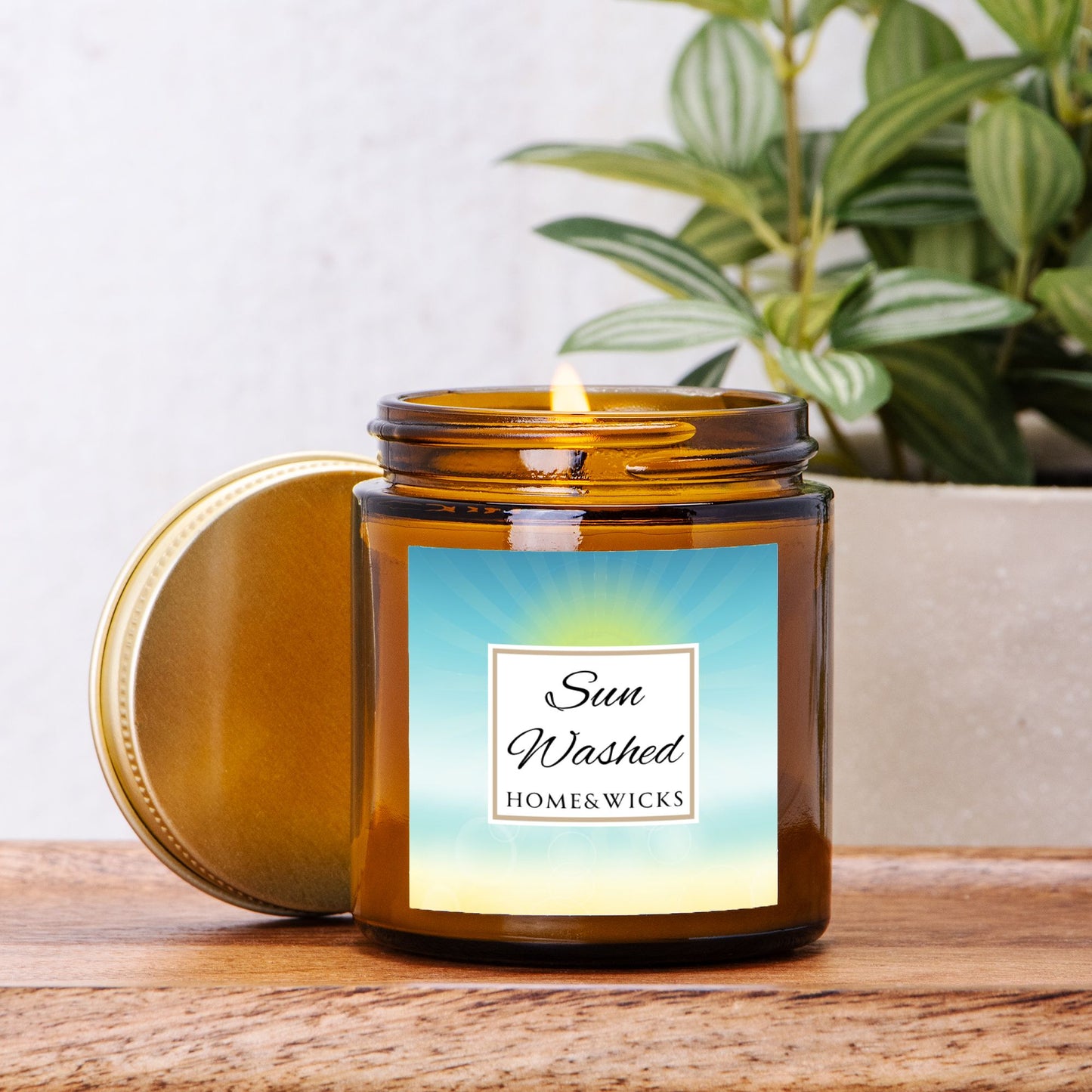 Sun Washed candle in a 4 oz. jar labeled 'Sun Washed' with sun graphic by Home & Wicks on a white background surrounded by greenery on a wooden surface.