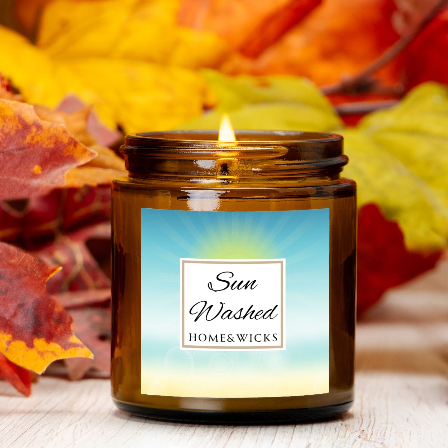 Sun Washed candle in a 4 oz. jar labeled 'Sun Washed' with sun graphic by Home & Wicks on a white background with autumn leaves in the background