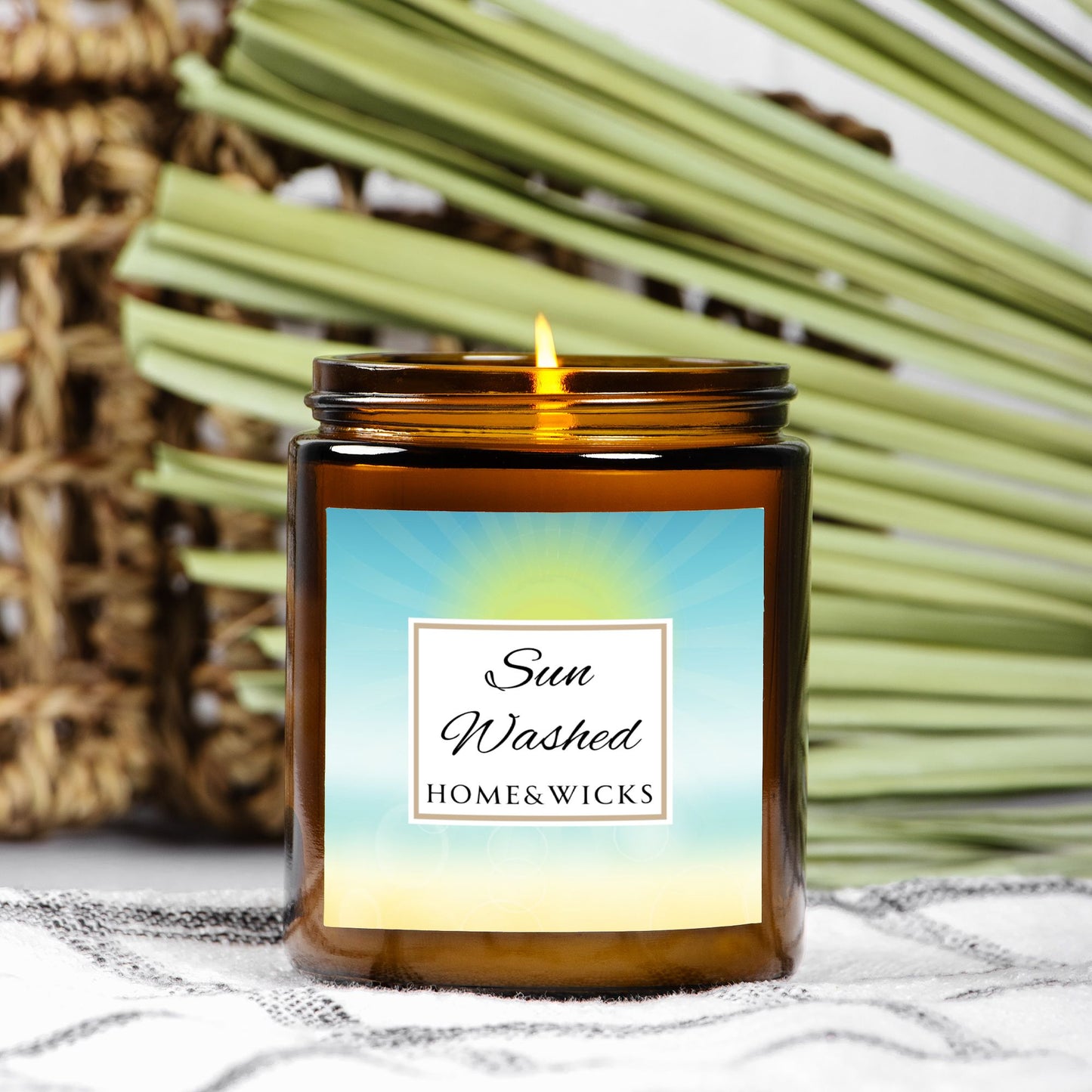 Candle in a 9 oz. amber jar with gold lid with 'Sun Washed' label on with sun graphic gradient background by Home & Wicks with a blurred natural background.