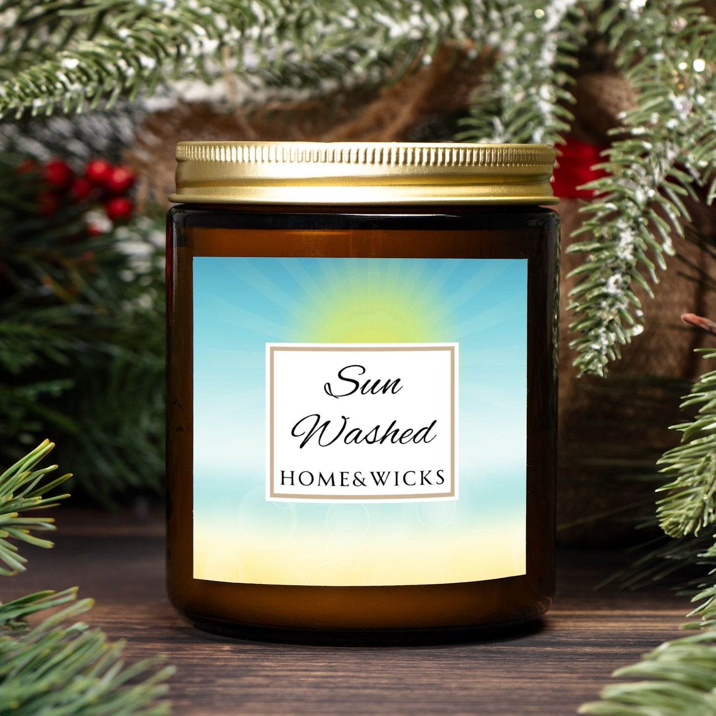 Candle in a 9 oz. amber jar with gold lid with 'Sun Washed' label on with sun graphic gradient background by Home & Wicks, surrounded by greenery
