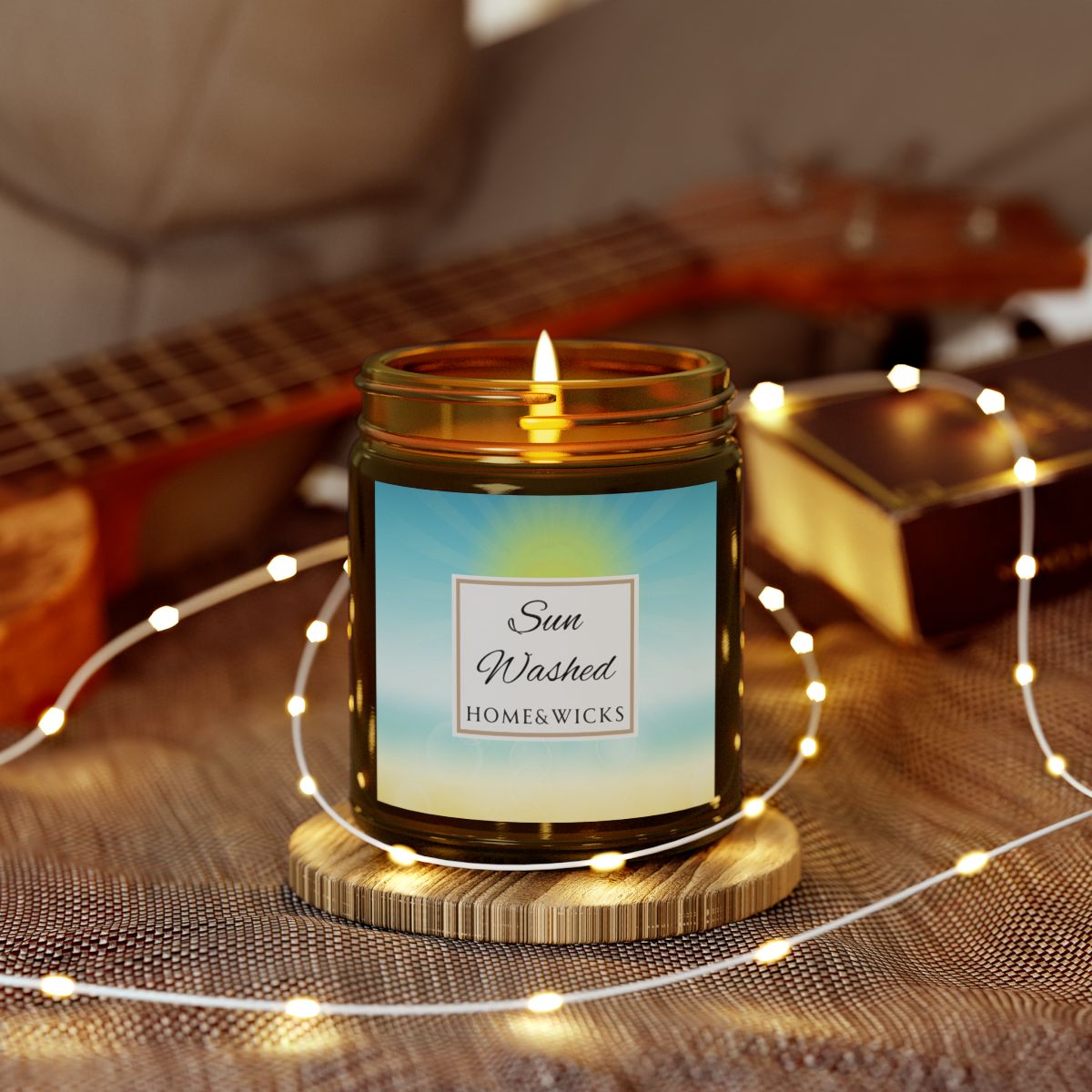 Candle in a 9 oz. amber jar with gold lid with 'Sun Washed' label on with sun graphic gradient background by Home & Wicks surrounded by string lights on a textured surface.