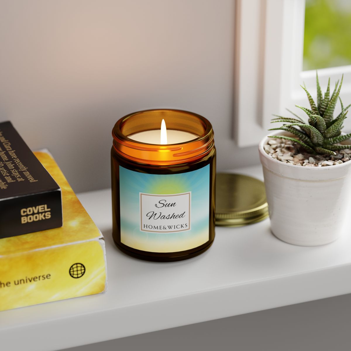 Candle in a 9 oz. amber jar with gold lid with 'Sun Washed' label on with sun graphic gradient background by Home & Wicks on a shelf with books and a plant.