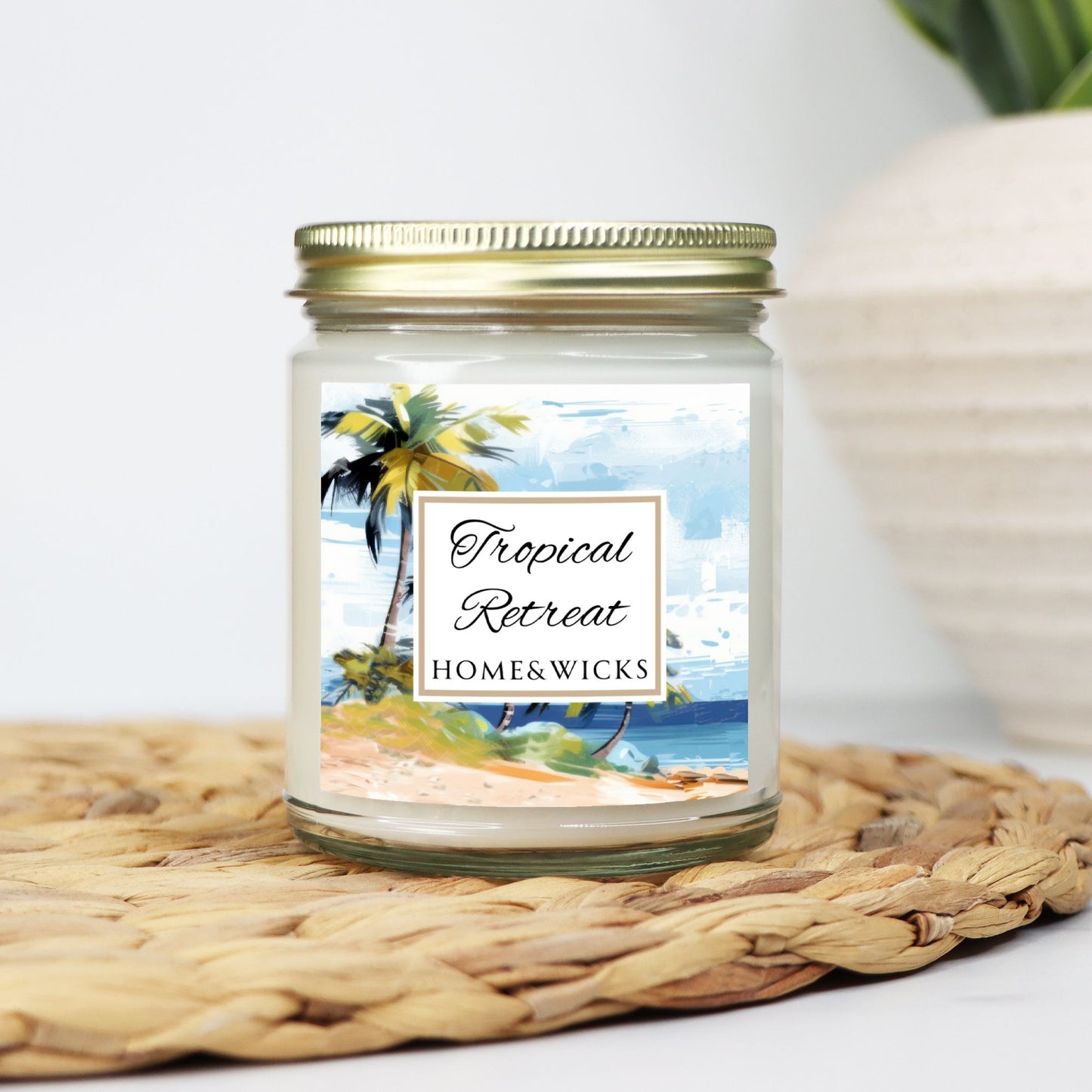 Tropical Retreat clear jar candle with gold lid labeled 'Tropical Retreat' with tropical beach seashore by Home & Wicks on a white background on a woven mat