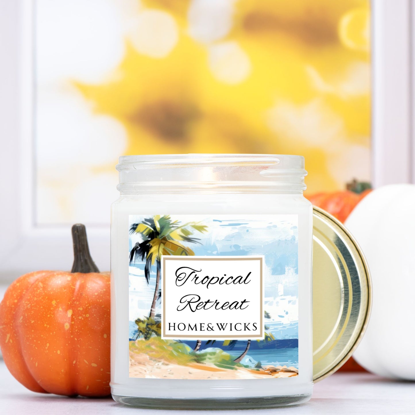 Tropical Retreat clear jar candle with gold lid labeled 'Tropical Retreat' with tropical beach seashore by Home & Wicks on a white background with pumpkins in the background.
