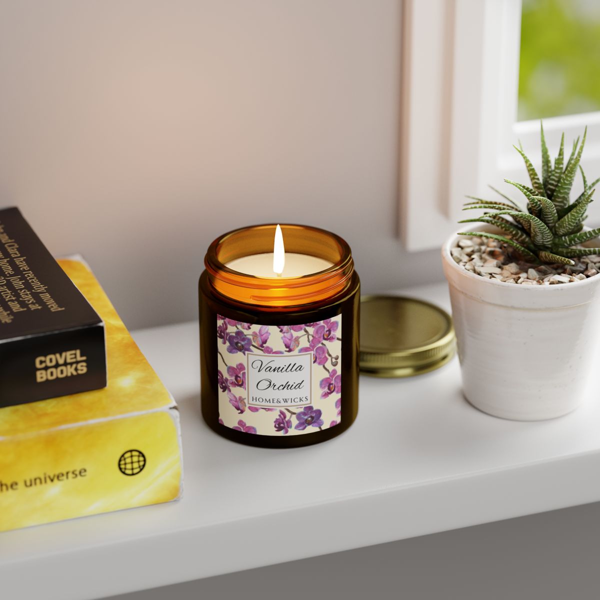 Vanilla Orchid candle in a 4 oz. amber glass candle jar with gold lid with a pink and purple orchid floral label on a white background by Home & Wicks on a shelf next to books and a plant