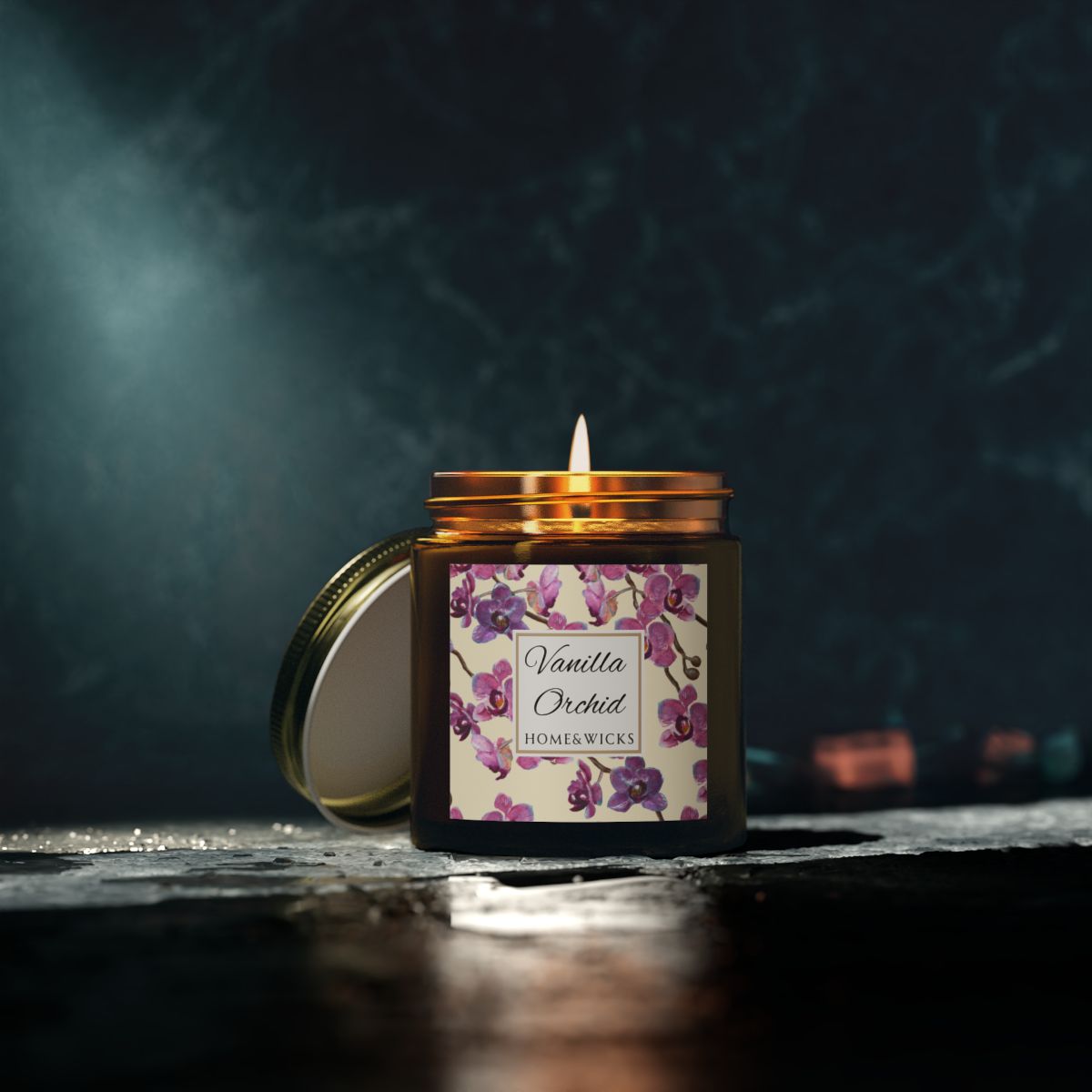 Vanilla Orchid candle in a 4 oz. amber glass candle jar with gold lid with a pink and purple orchid floral label on a white background by Home & Wicks on a dark background