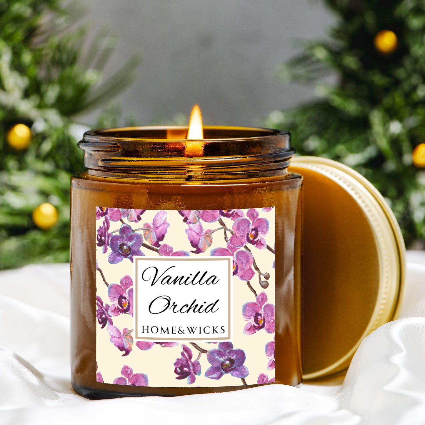 Vanilla Orchid candle in a 4 oz. amber glass candle jar with gold lid with a pink and purple orchid floral label on a white background by Home & Wicks on a white surface with orange trees in the background