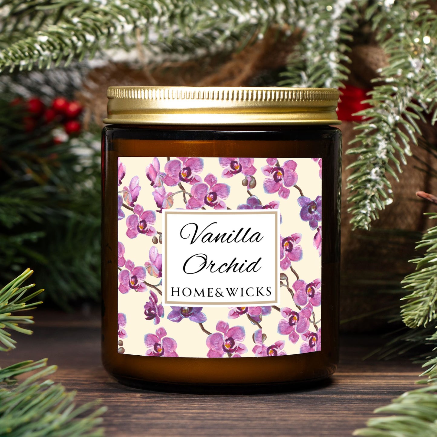 Vanilla Orchid candle in an amber jar with gold lid with a pink and purple orchid design label by Home & Wicks, surrounded by greenery.