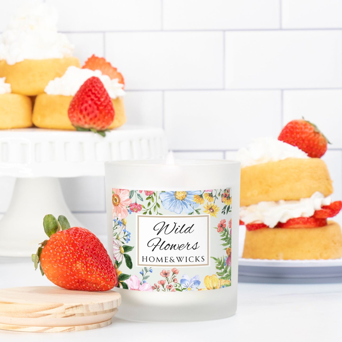 Candle labeled 'Wild Flowers Home & Wicks' with strawberry and cake decorations on a white tiled background