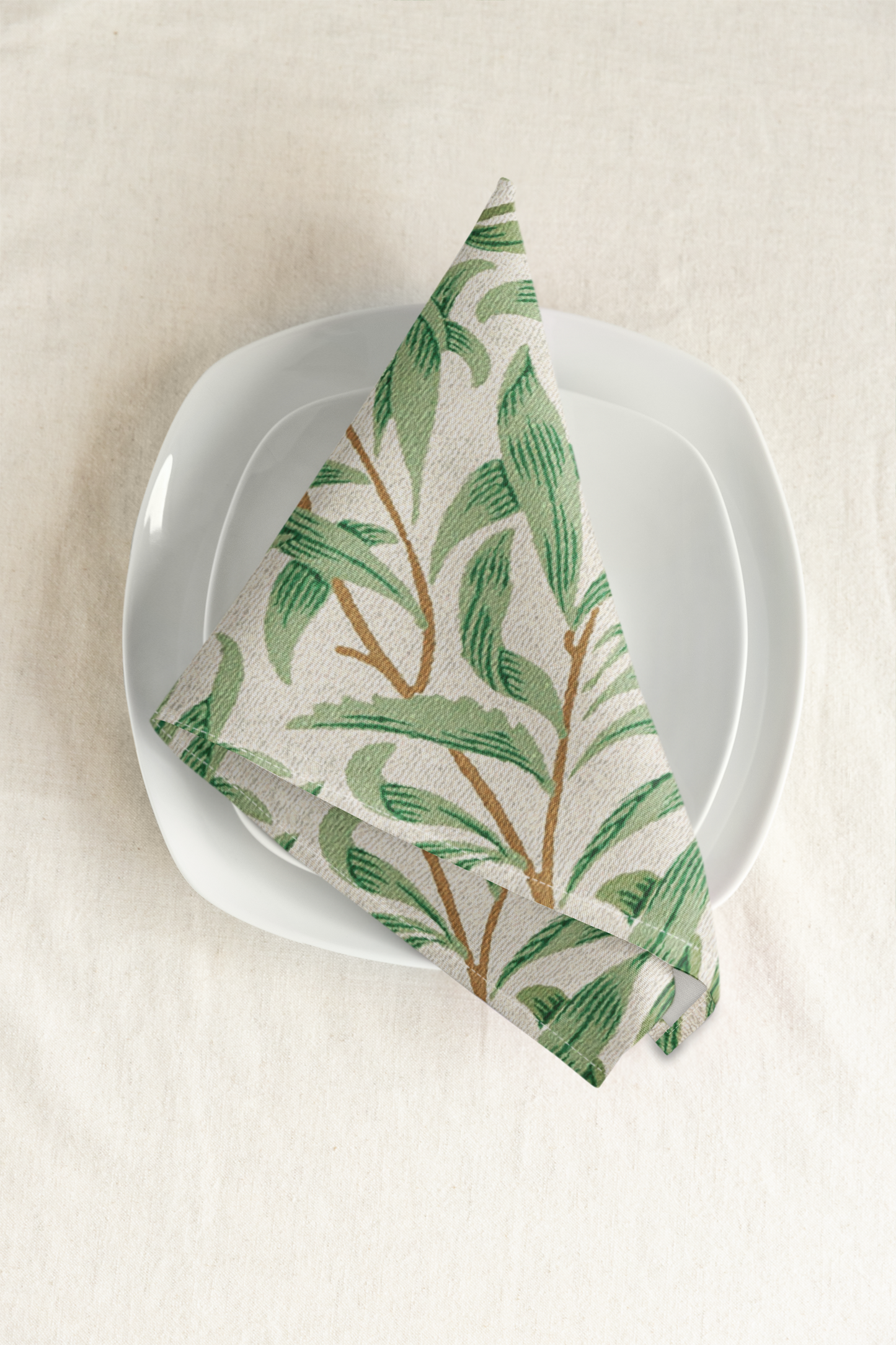 Willow Boughs 22 x 22 Napkin with green leaf willow branch pattern on a white plate against a beige background