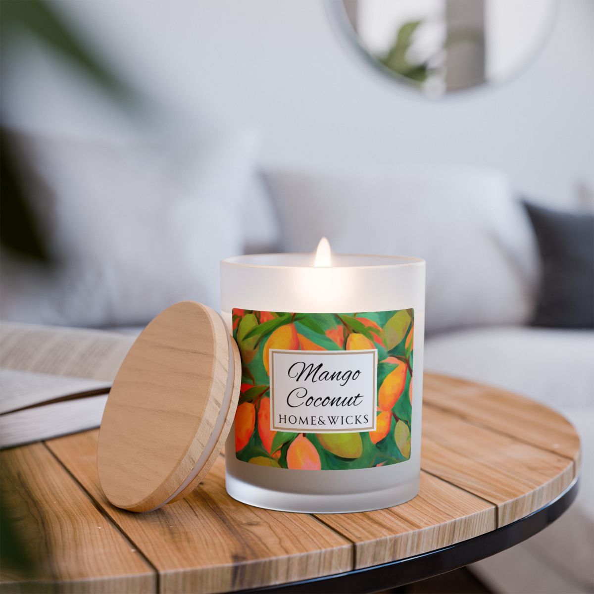 Lit wood wick candle with a green and orange mango coconut label on a frosted glass candle jar on a white background by Home & Wicks on a wood table