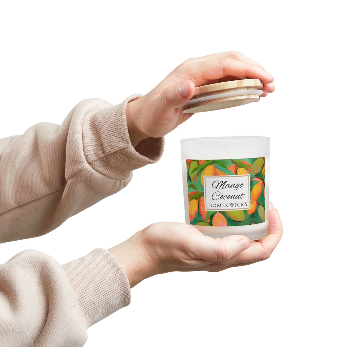 Person holding a frosted jar candle labeled 'Mango Coconut' by Home & Wicks on a white background