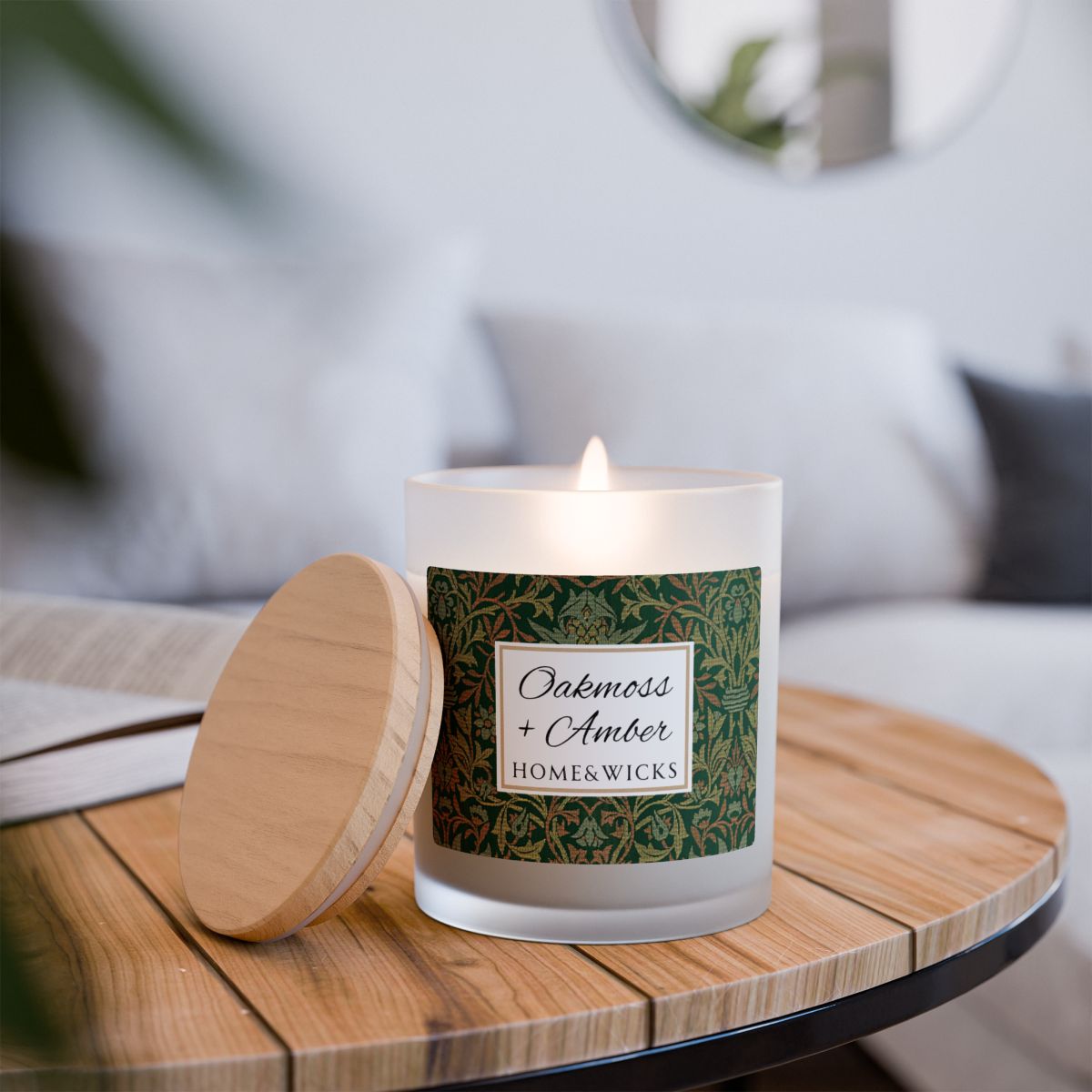 Wood wick Oakmoss & Amber candle in a frosted glass jar with a green decorative label featuring the illustration by William Morris "Flower Garden" on a white background on a wooden table in a home setting