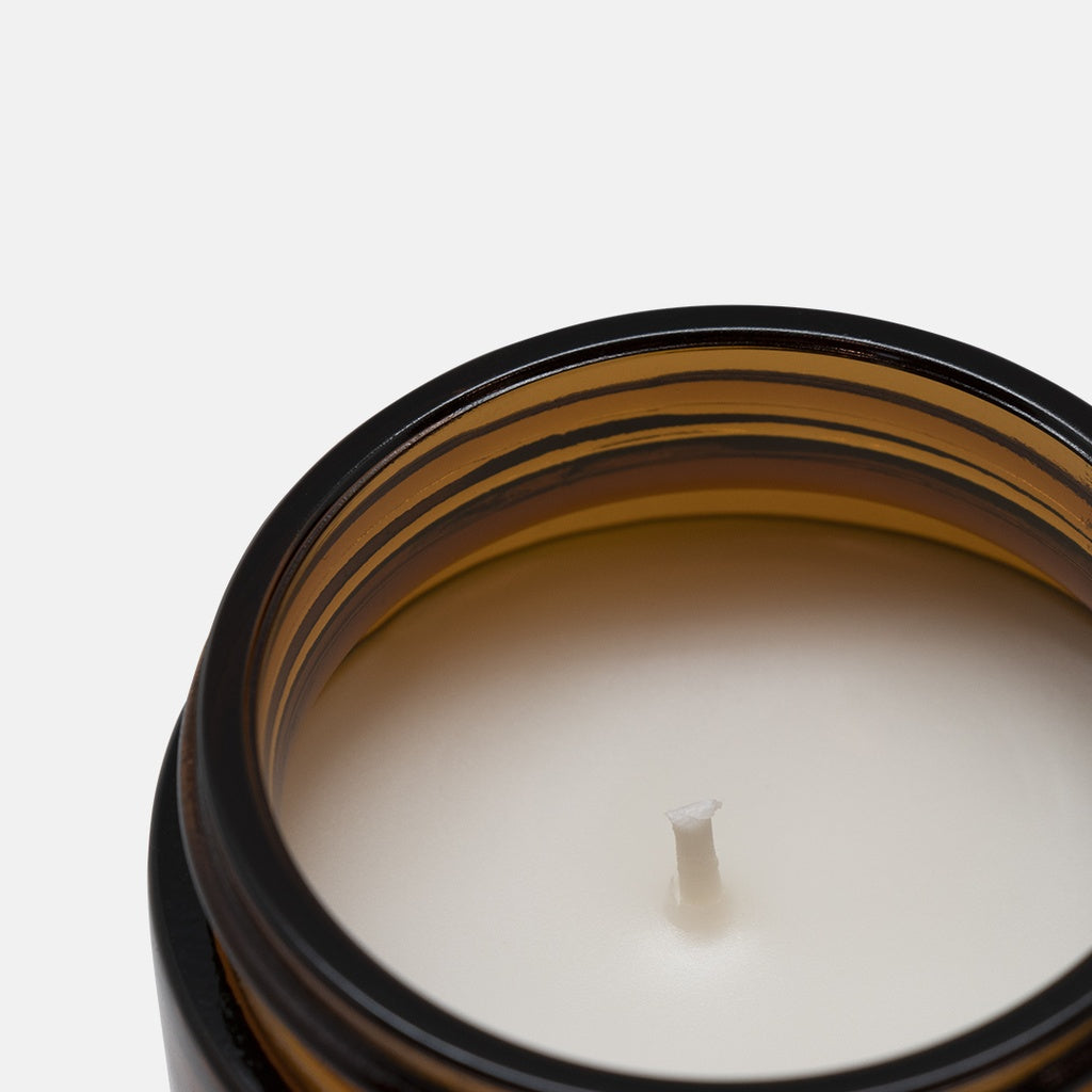 Close-up of a white candle in a amber container with cotton wick on a white background