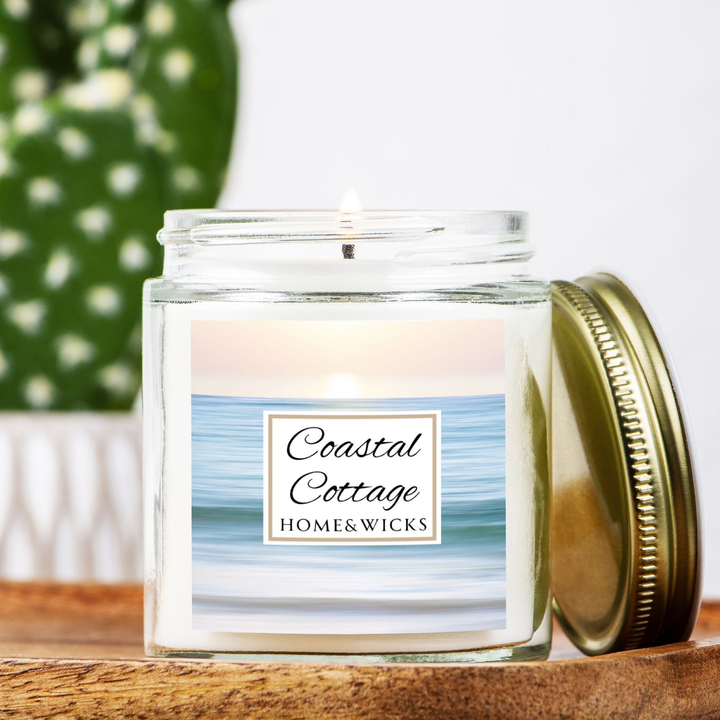 Coastal Cottage candle jar with a label reading 'Coastal Cottage' by 'Homes & Wicks' with a calm ocean shore image on a white background on a wooden surface, featuring 'Coastal Cottage Home & Wicks'.