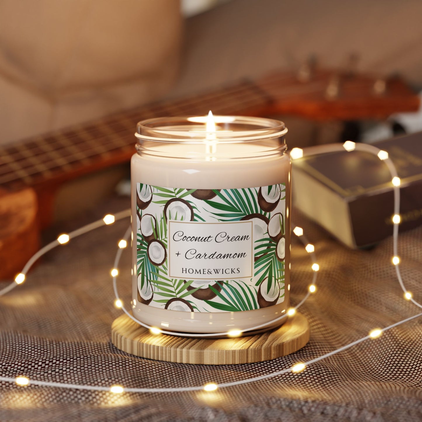 Candle with a coconut cream and cardamom label on a wooden coaster with string lights in the background.