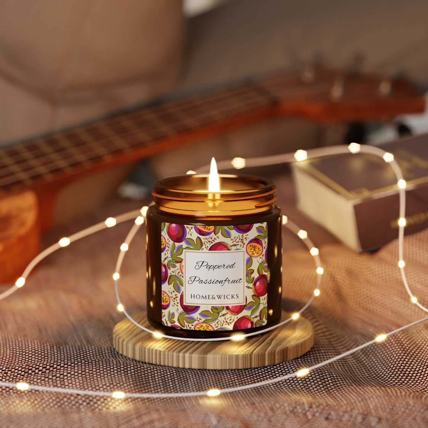 Home and Wicks peppered passionfruit candle with decorative label on a wooden coaster surrounded by string lights, with a guitar in the background.