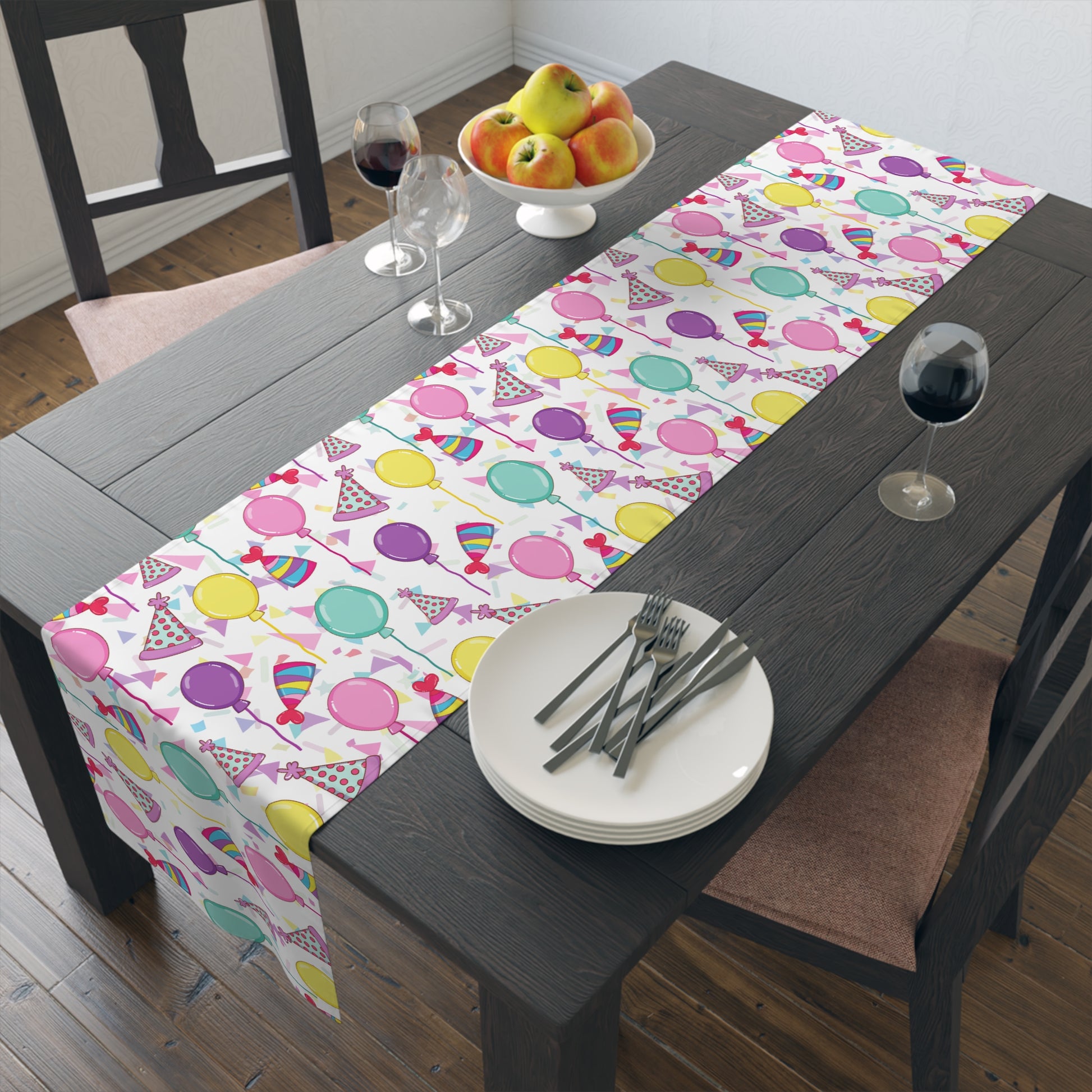 Table runner with birthday hats, confetti and purple, yellow, blue and pink balloons on a white background on a dark wood table 