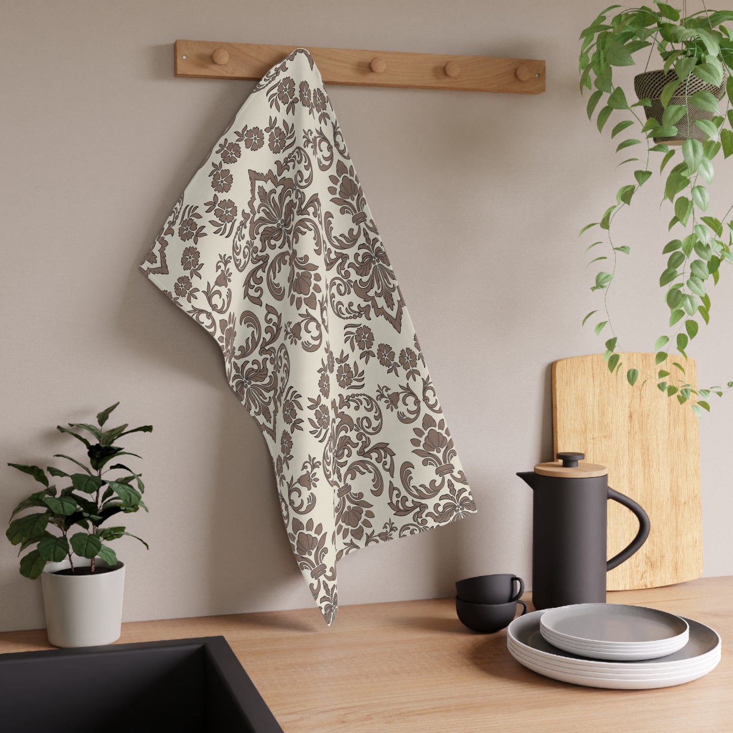 Decorative baroque mocha kitchen tea towel with floral pattern hanging on a wooden rack above a kitchen counter with utensils and plants.
