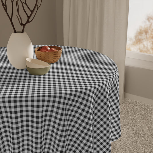 Round table with a black and white gingham checkered tablecloth, vase, and basket in a room.