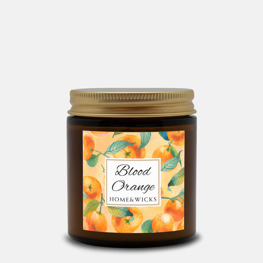 Blood Orange candle in an amber glass jar with gold lid with 'Blood Orange' label featuring oranges illustration on a white background by Home & Wicks