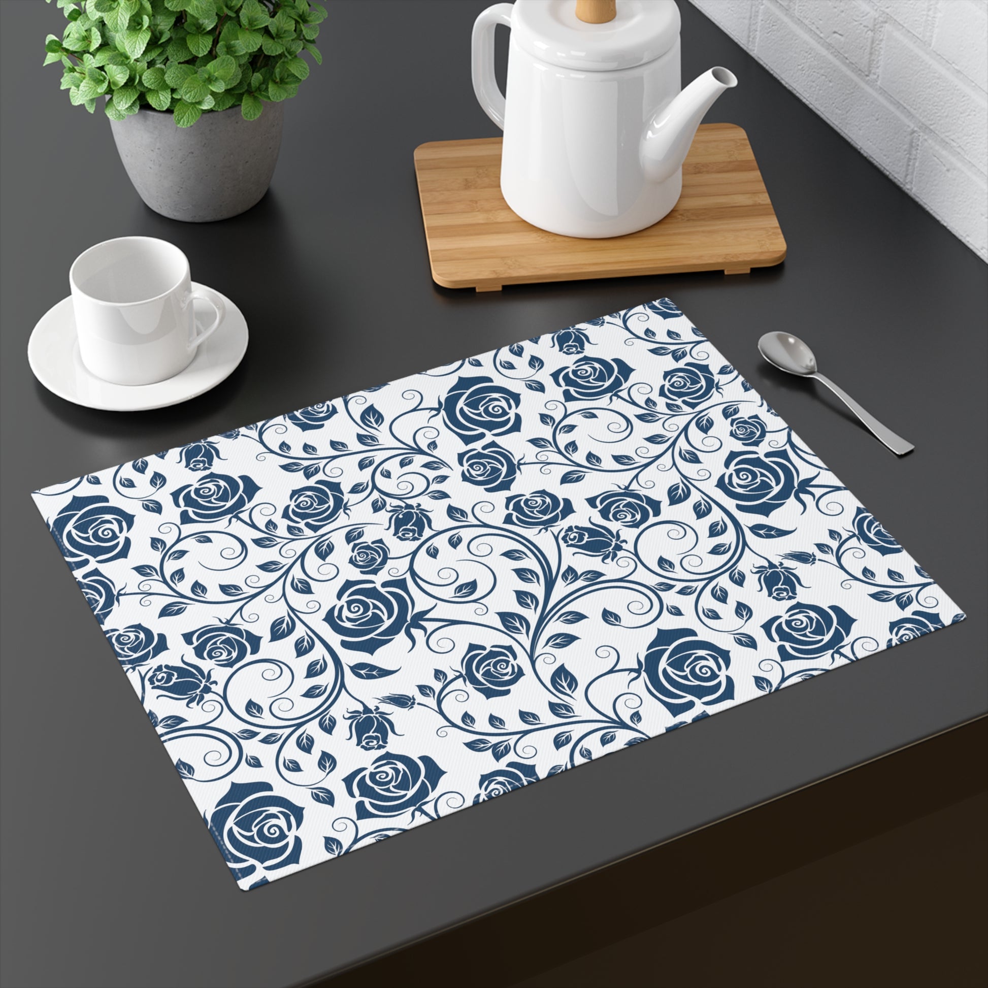 Placemat with blue rose pattern on a dark surface with tea set and plant.