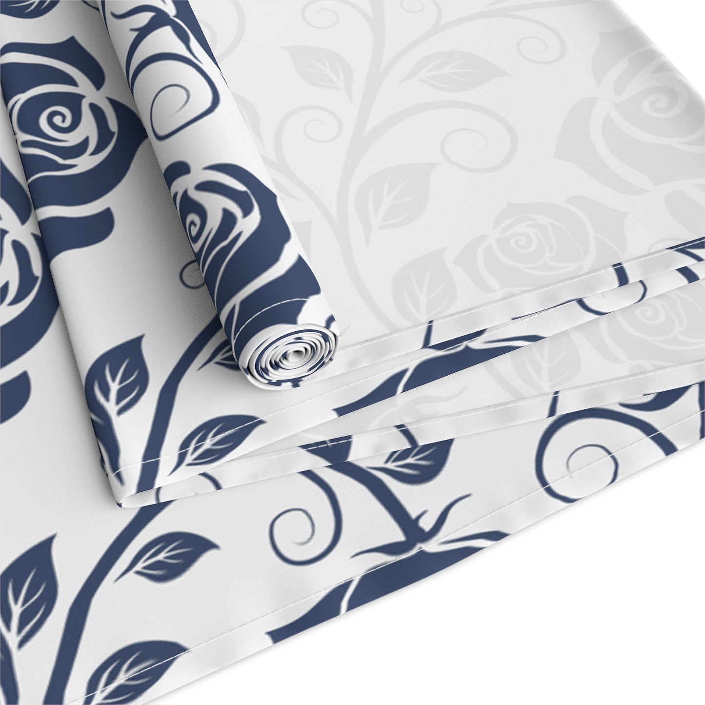 Table runner with blue and white floral pattern rolled up and folded on a white background