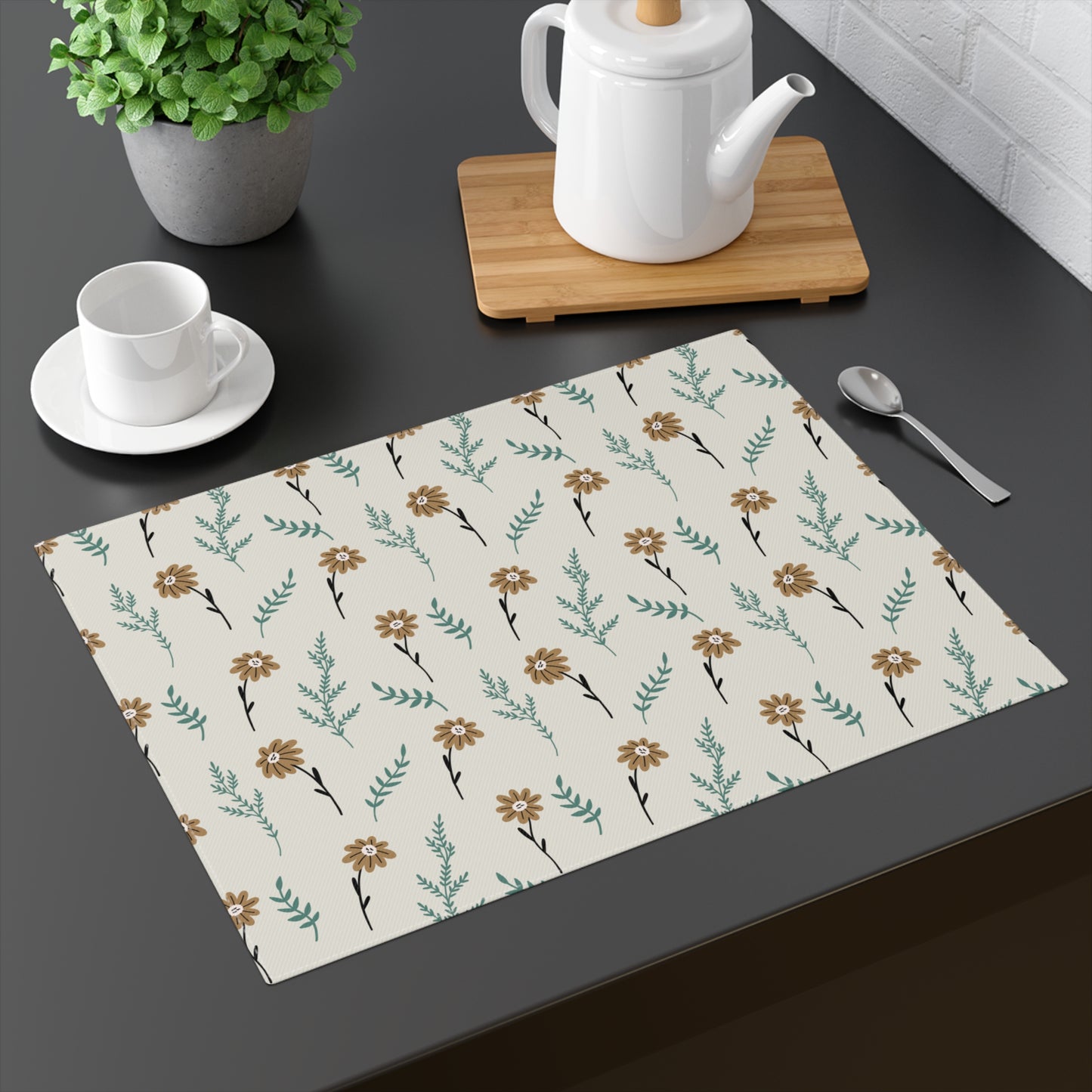Our Brown Camomile placemat with brown and gray floral pattern on cotton twill fabric with small flowers and leaves on a beige background on a dark surface with tea set and plant.