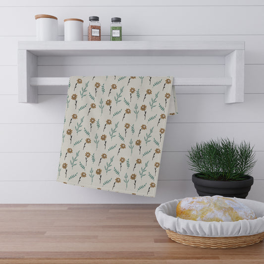 Brown floral-patterned kitchen tea towel hanging on a wooden shelf with a plant and basket in the foreground.