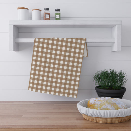 Brown gingham checkered kitchen tea towel hanging on a shelf above a wooden surface with a basket and plant.