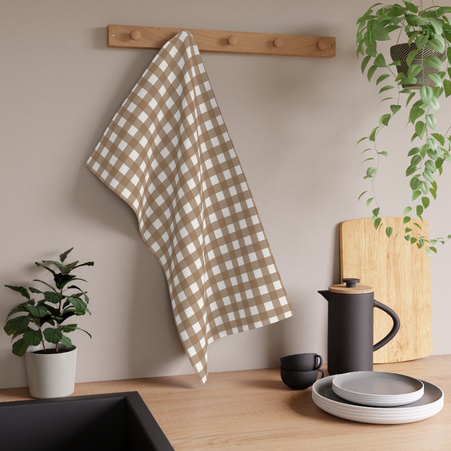 Brown gingham checkered kitchen tea towel hanging on a wooden rack above a kitchen counter with plants and utensils.