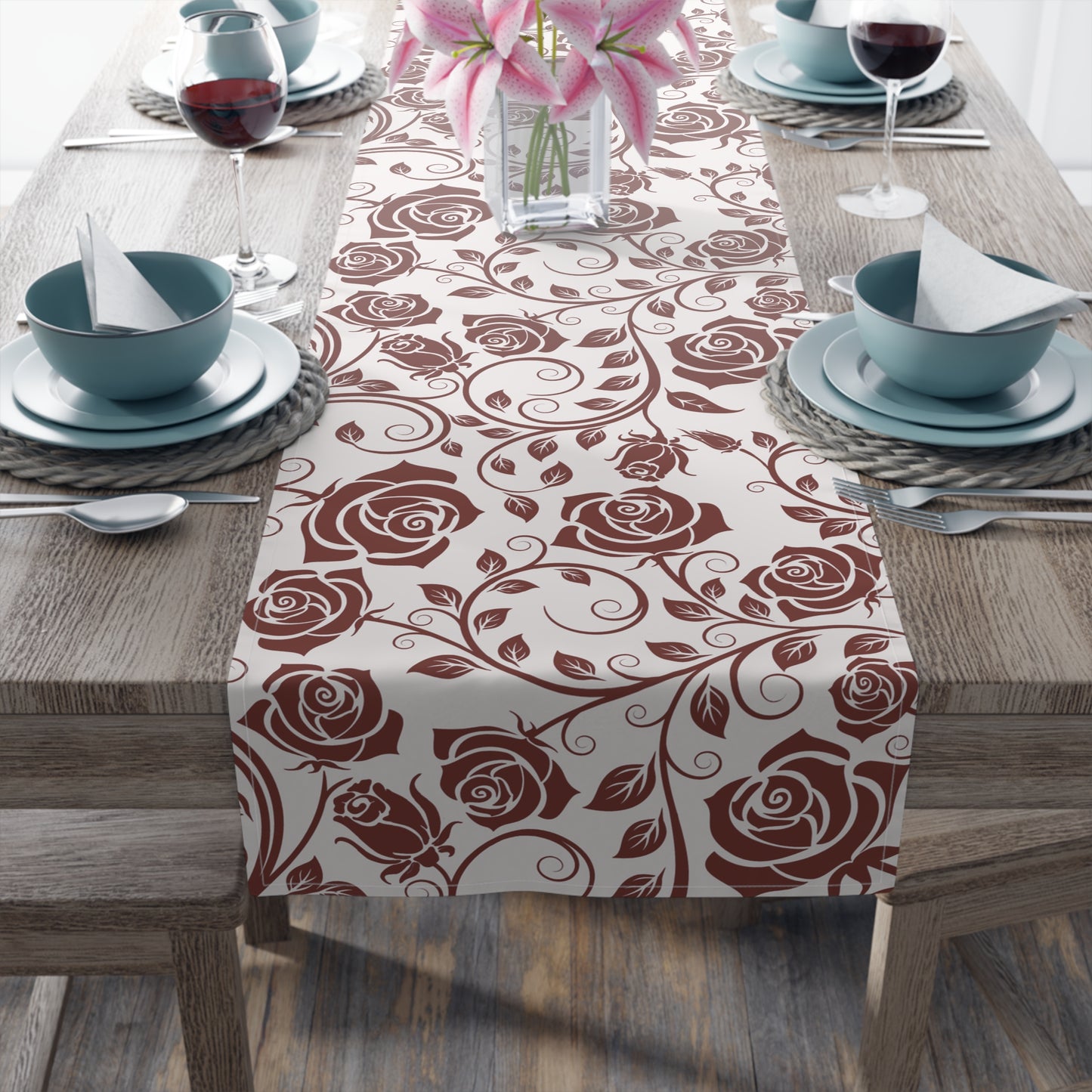 Table setting with a burgundy floral table runner on a wooden table.