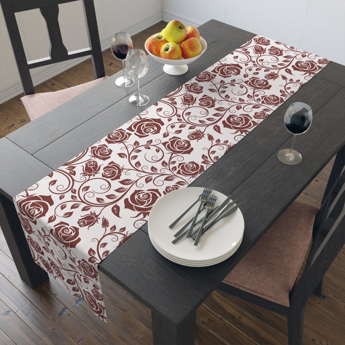 Dining table with a burgundy floral table runner, plates, and cutlery.