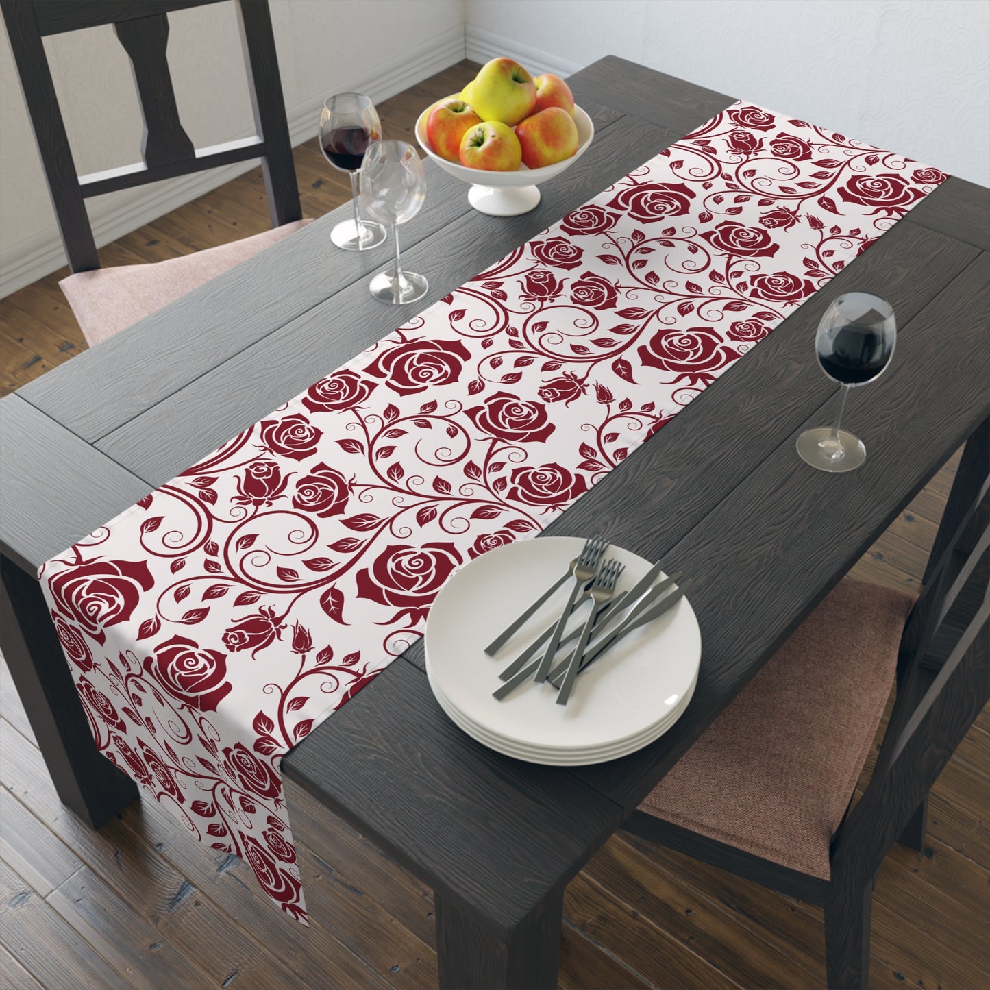 Dining table with a red rose patterned table runner, plates, cutlery, and fruit.