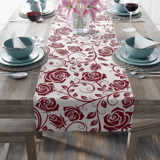 Table setting with a red rose patterned table runner on a wooden table.