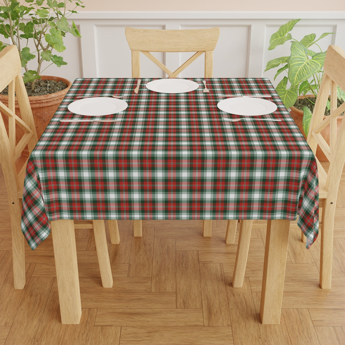 Dining table with a red and green plaid tablecloth, white plates, and wooden chairs.