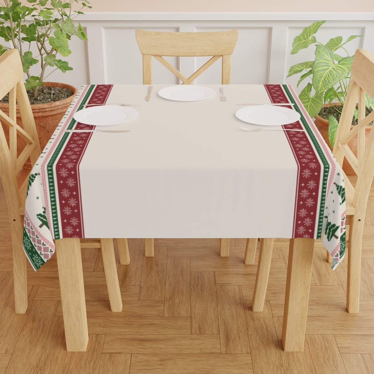 Dining table with a beige decorative tablecloth featuring green and red Christmas trees and snowflakes pattern, and chairs on a wooden floor.