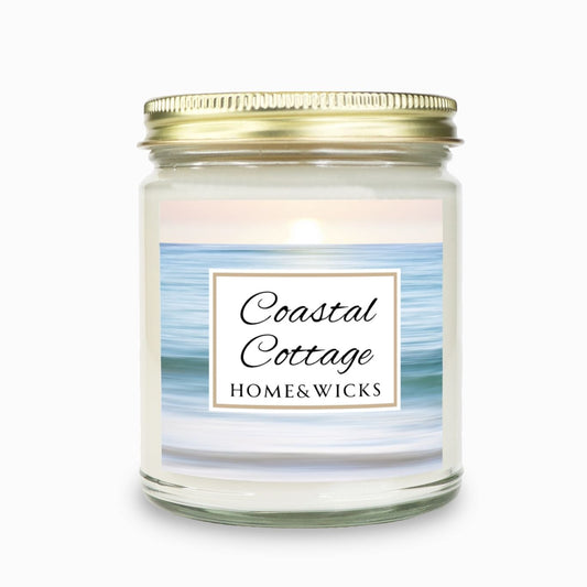 Coastal Cottage candle in clear jar with gold lid with a 'Coastal Cottage Home & Wicks' label with ocean shore image on a white background