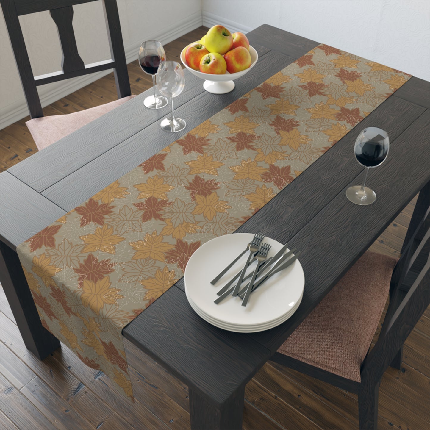 Dining table with a fall leaf-patterned table runner, plates, forks, and a fruit bowl.