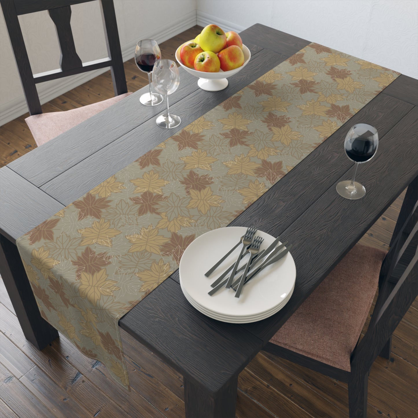 Dining table with a leaf patterned table runner, plates, forks, and a fruit bowl.