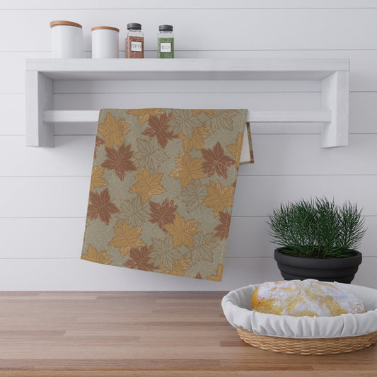 Decorative tea towel with autumn leaf pattern on a wooden rack with a plant and basket.