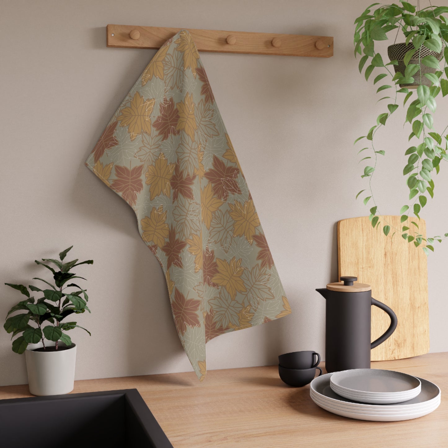 Kitchen scene with a leaf patterned towel hanging on a rack, plants, and kitchenware.
