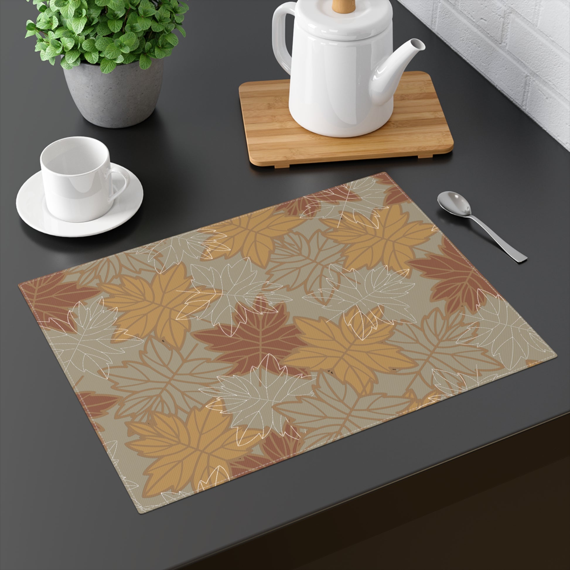 Our Earthy Leaves placemat with a brown, gold and olive green-gray autumn leaf pattern on a dark surface with tea set and plant.