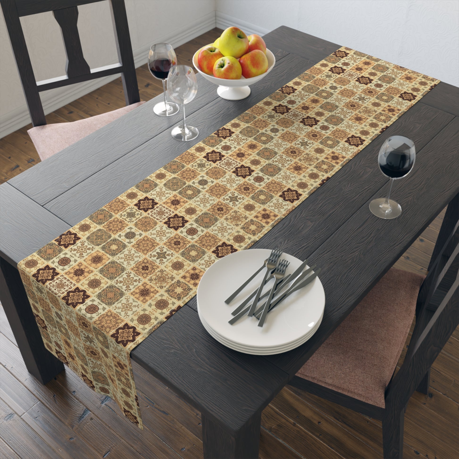 This Fall Flowers Mosaic table runner has a brown, green and gold floral square geometric pattern. This table runner is on a dining table with plates, forks, and a fruit bowl.